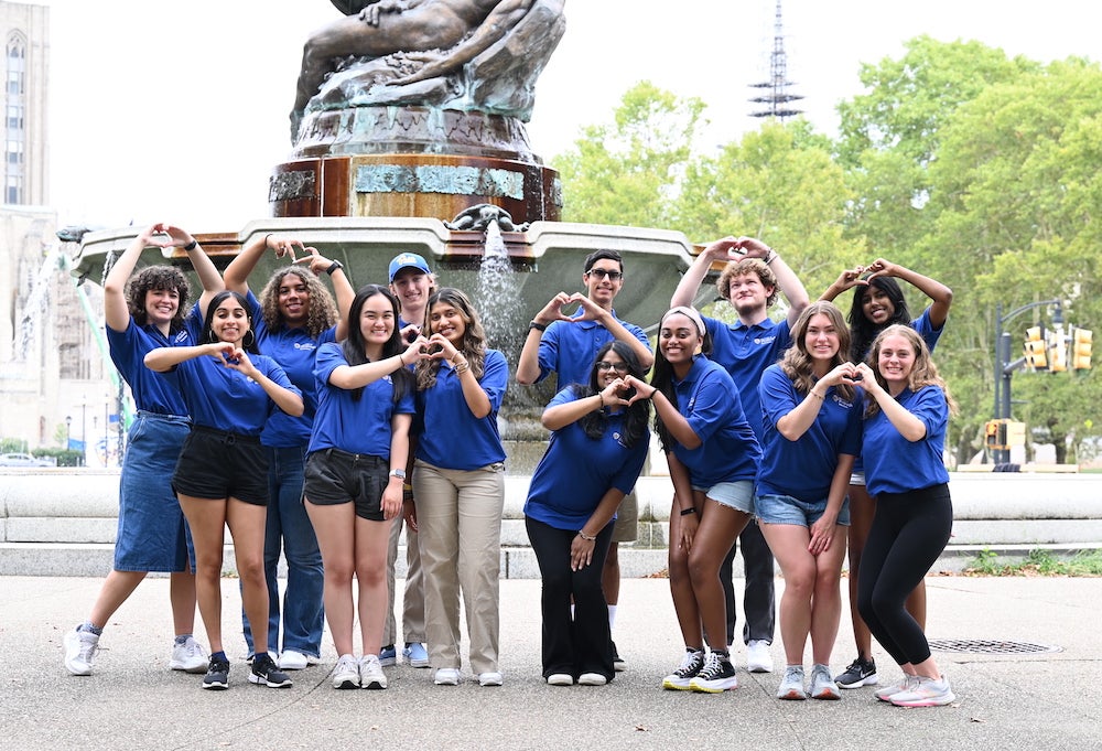 "Student ambassadors pose making heart shapes with their hands in front of a fountain"
