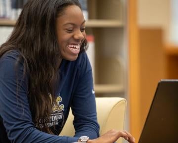 young woman smiles while using a laptop