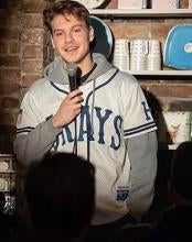 Man stands against a brick wall holding a microphone